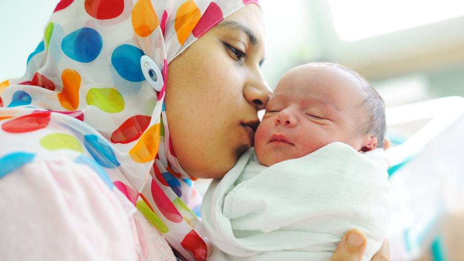 a mother wearing a hijab holding her infant, newborn baby wrapped in a blanket