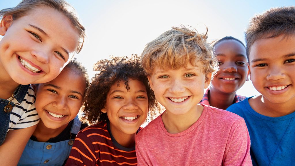 a group of happy children laughing and smiling outside in the sunshine