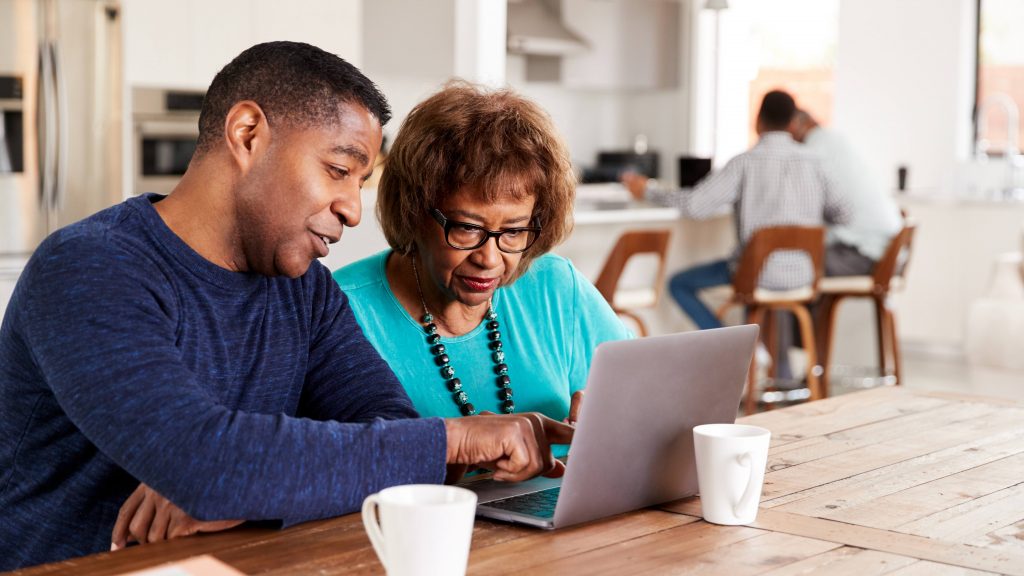 a middled-aged man helping an older woman with something on the screen of a laptop
