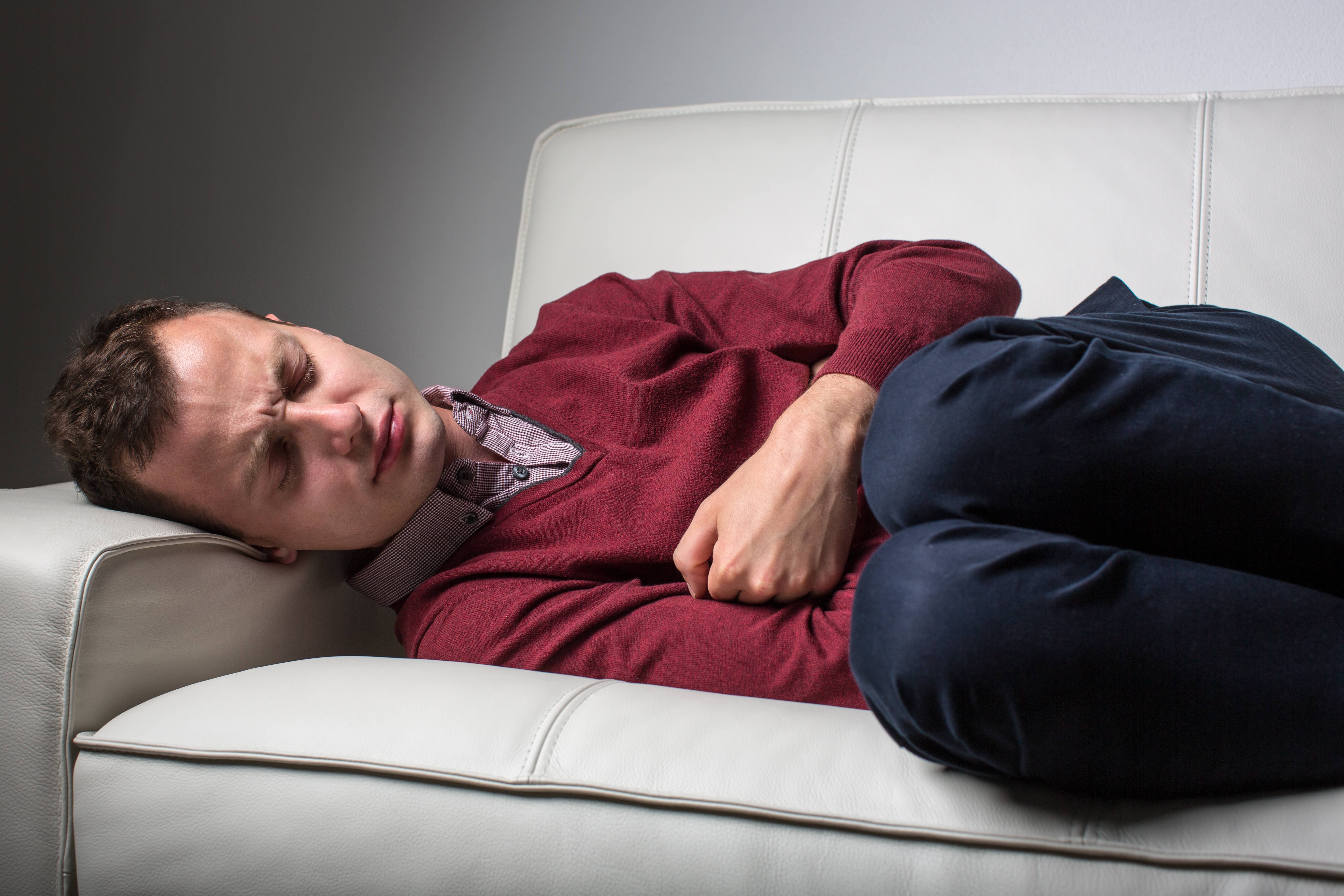 man lying on a couch suffering from severe stomach pain