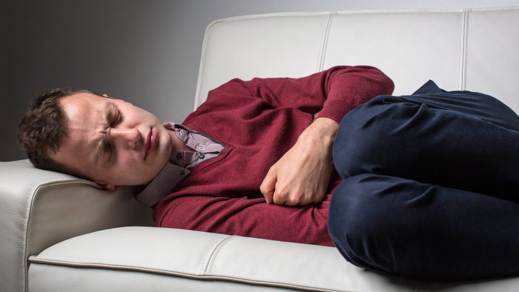 Un hombre recostado en un sofá con fuerte dolor de estómago