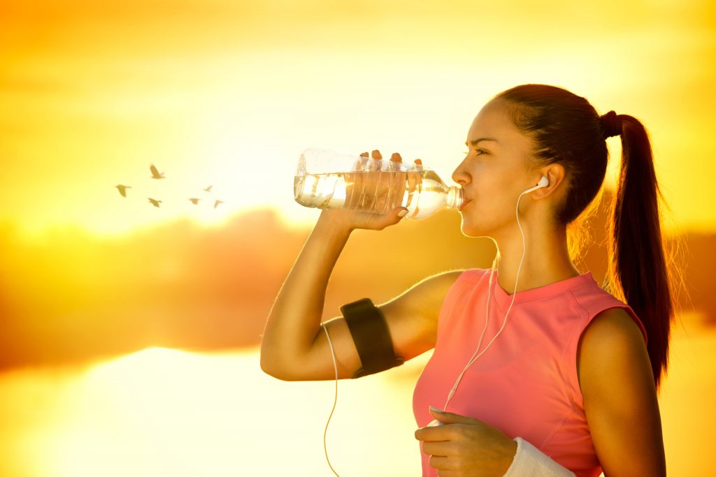 a young woman outdoors on a sunny day, drinking water and dressed for running