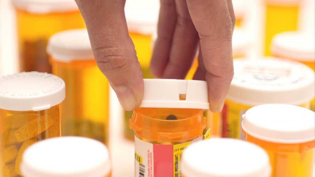 several prescription medicine pill bottles with a person's hand taking off one of the lids