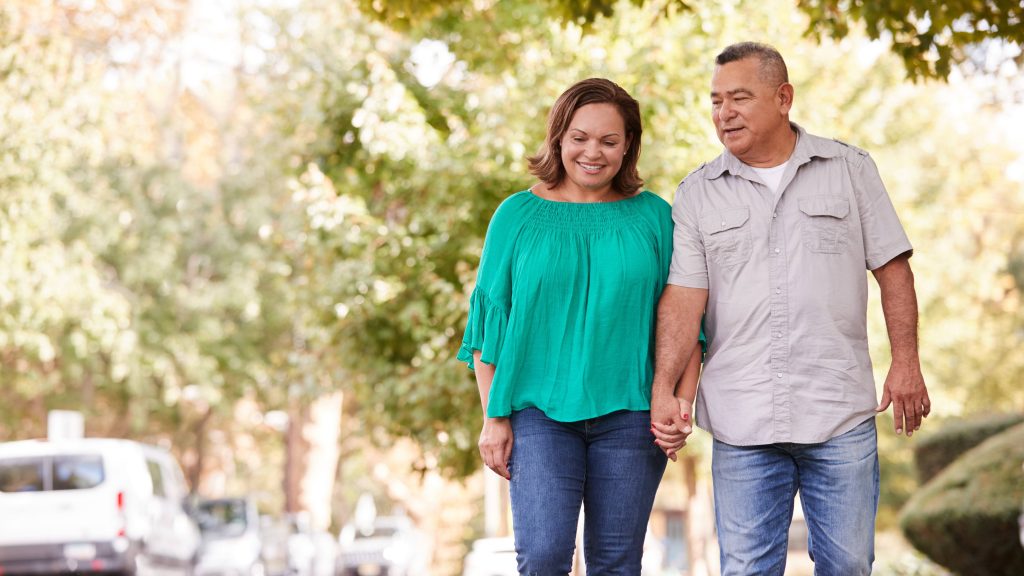 Senior couple walking along suburban street holding hands