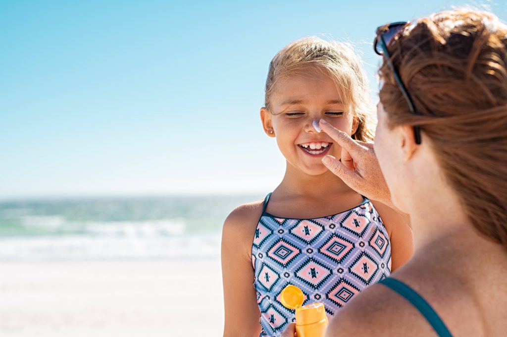 a woman applying sunscreen to the nose of a laughing young girl at the beach