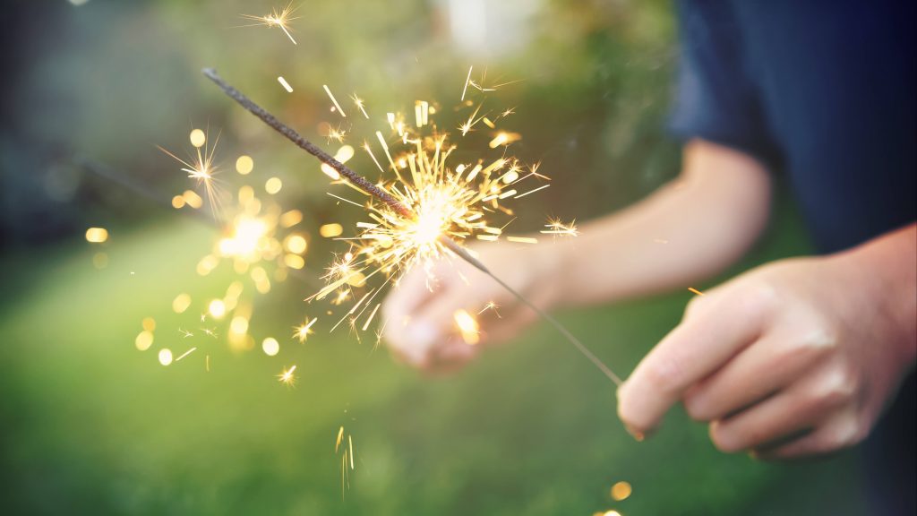 a young person lighting a fireworks sparkler in their hands