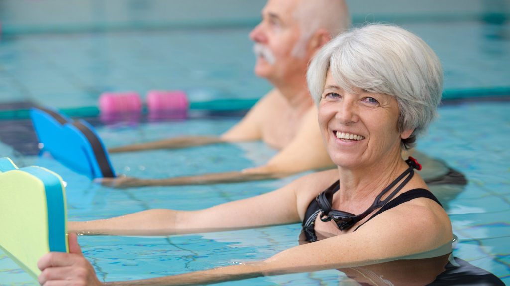 a smiling older woman in the pool in a swimming or aqua, water fitness class