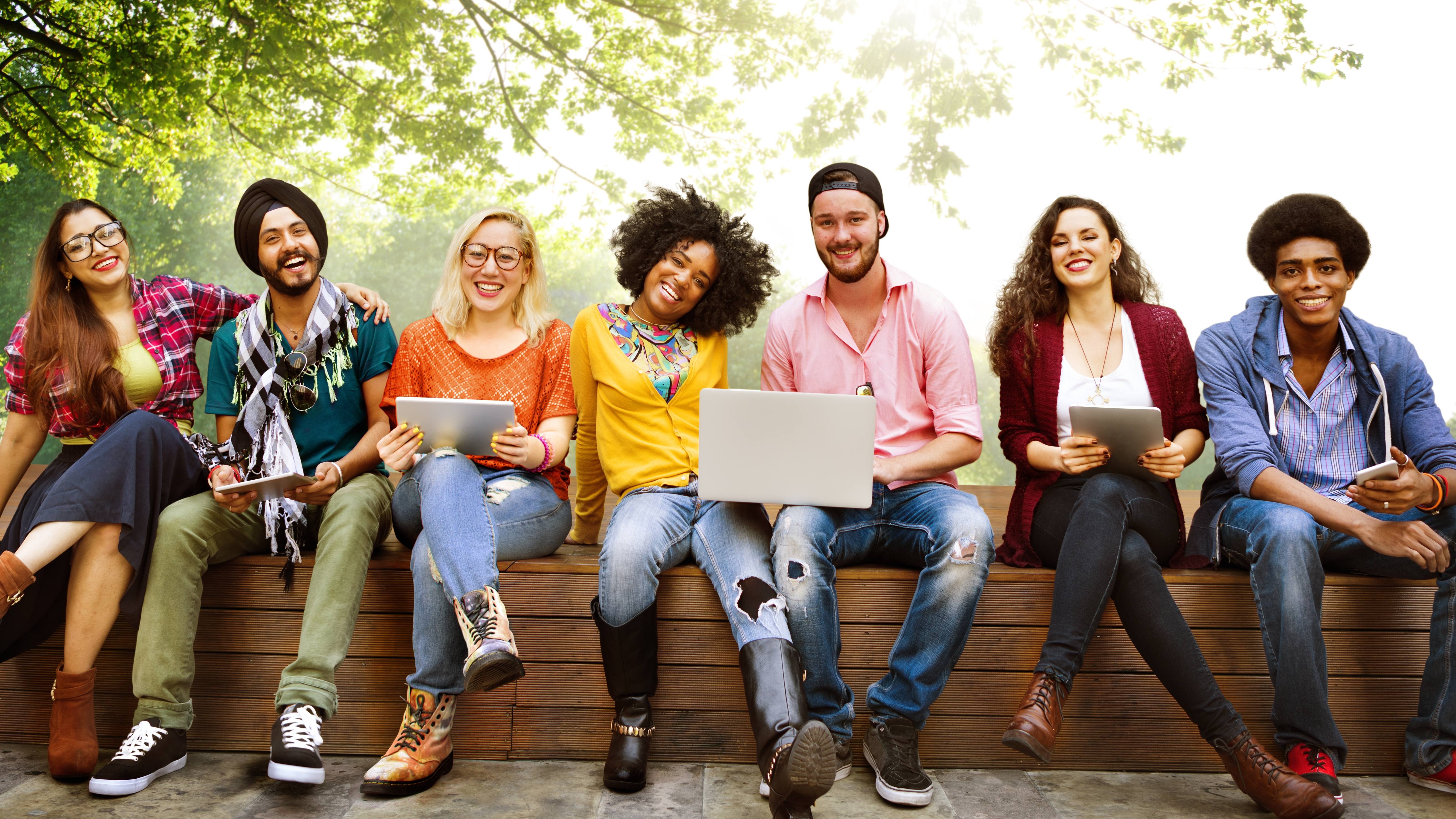 a diverse group of young people, students, artists, laughing and smiling as they work on laptops and computers