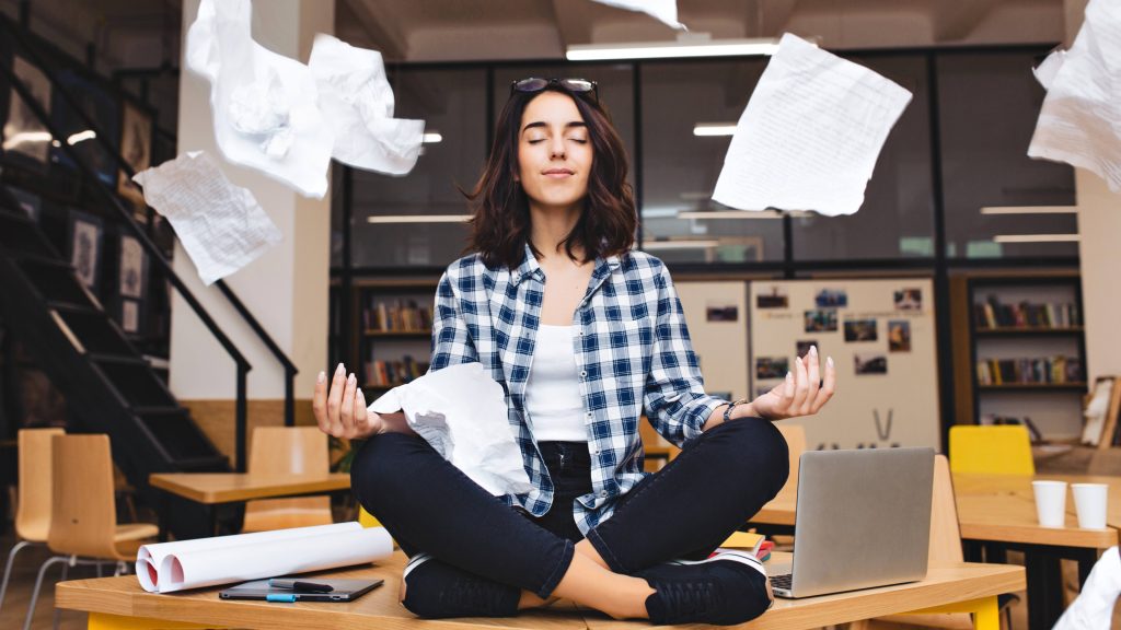 a young woman deep in thought, meditating on an office desk with work papers floating in the air