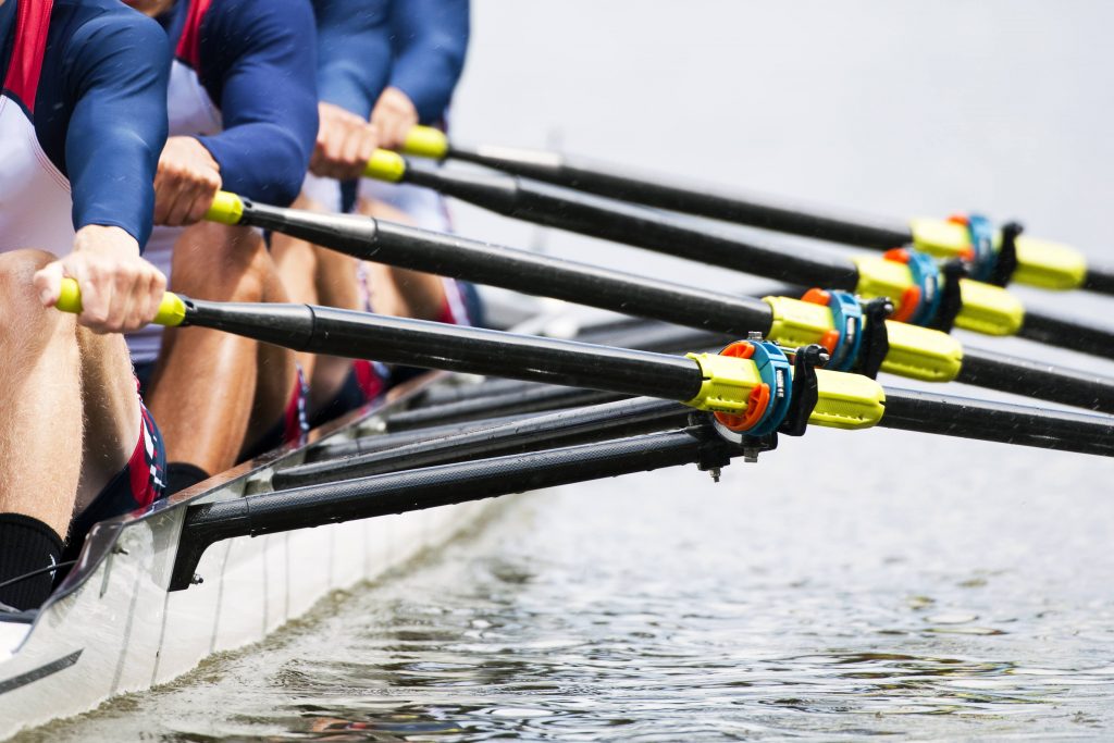 a sports rowing team in their shell or boat, paddling on the water, exercising and racing as a team