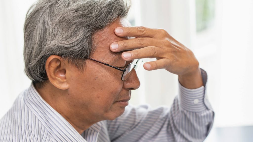 a middle-aged man wearing glasses and holding his hand to his head,looking sad and worried, maybe depressed and trying to remember something