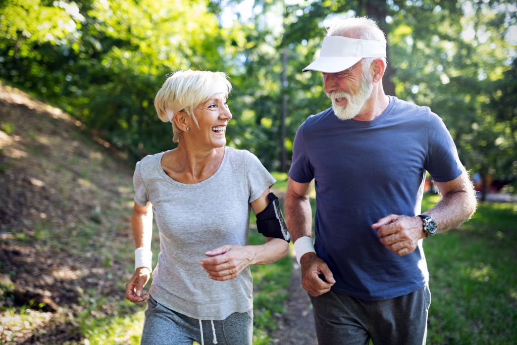 a happy, smiling older couple running on a path in a sunny park