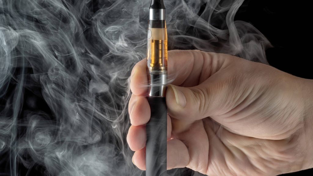 a person's hand holding an electronic cigarette, vaping e-cigarette, over a dark background with smoke billowing around it