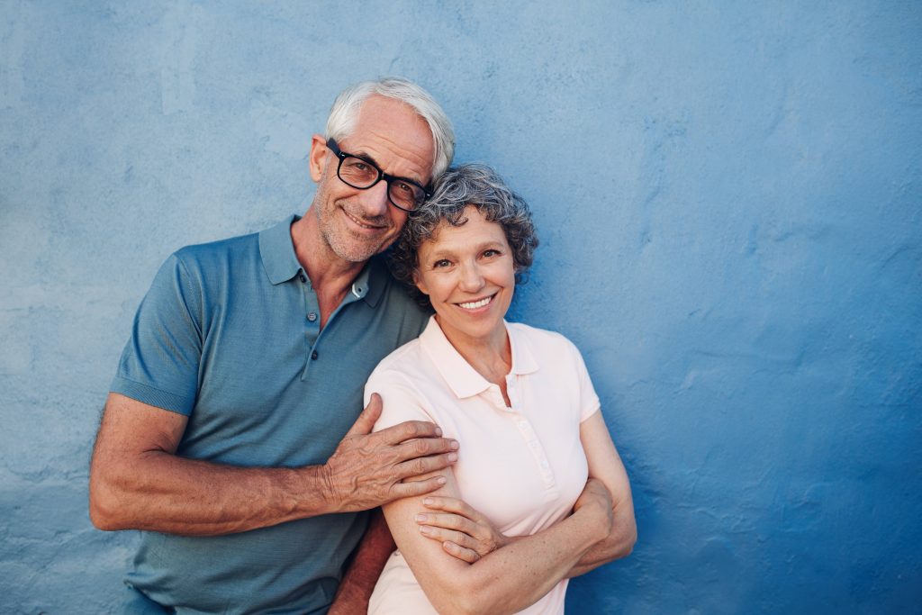 a happy, smiling middle-aged couple standing together in front of a blue wall