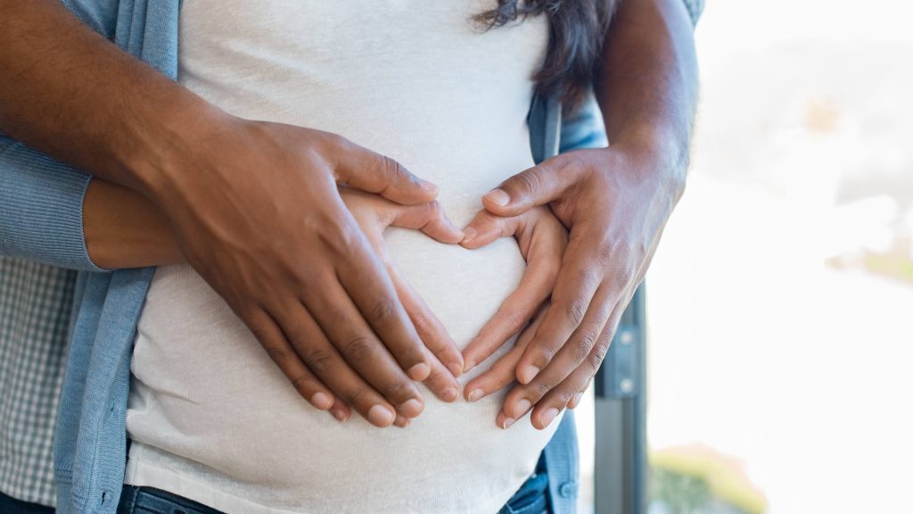 a pregnant woman with her partner placing their hands on her stomach in the shape of a heart