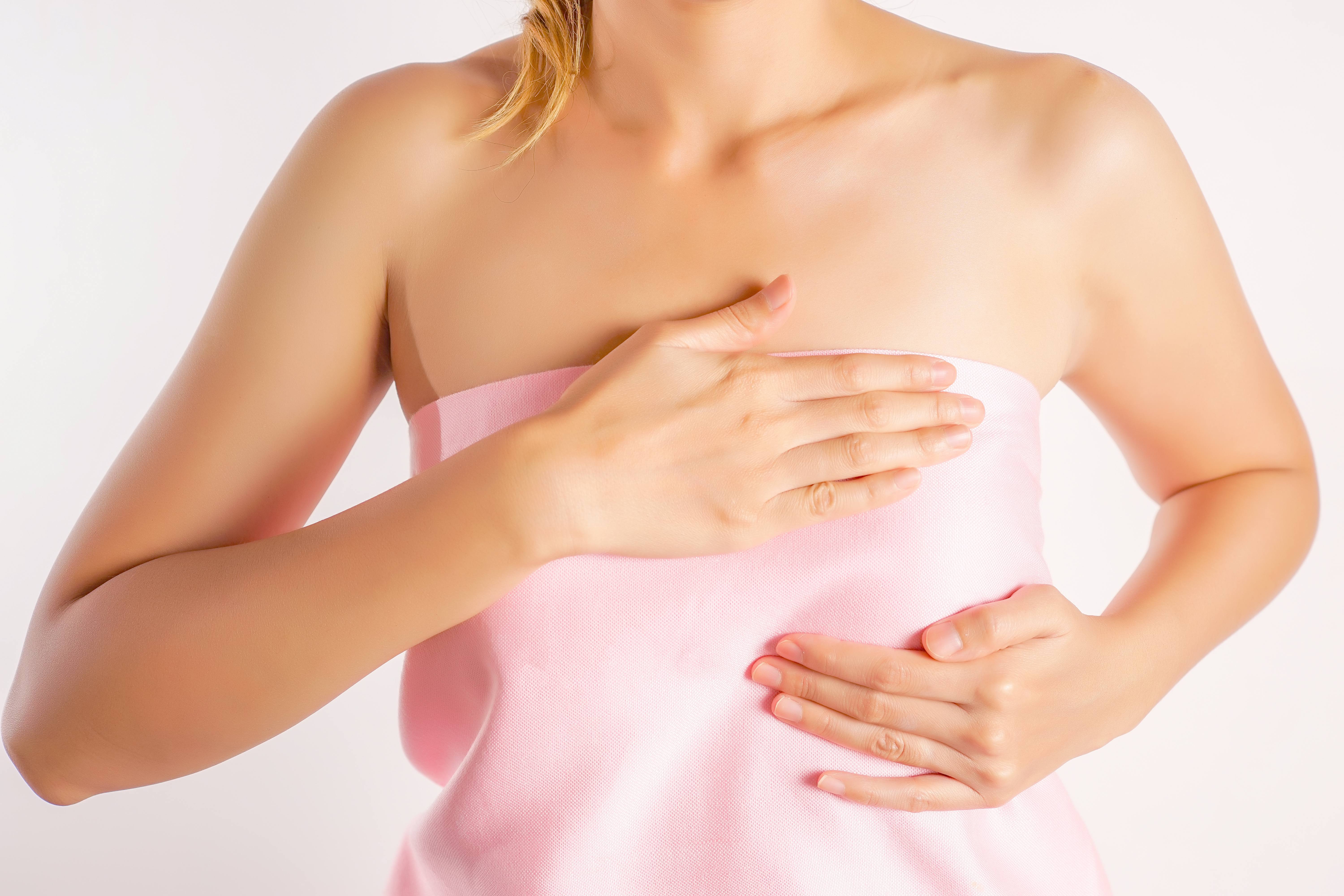 woman wearing a pink strapless shirt doing a breast self-exam