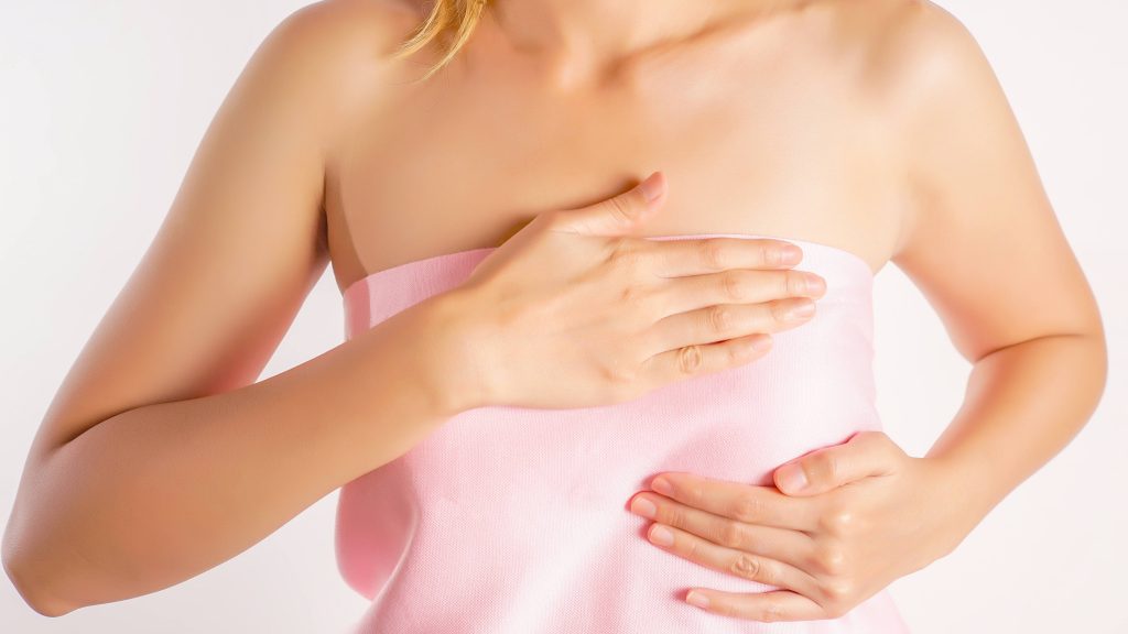 woman wearing a pink strapless shirt doing a breast self-exam