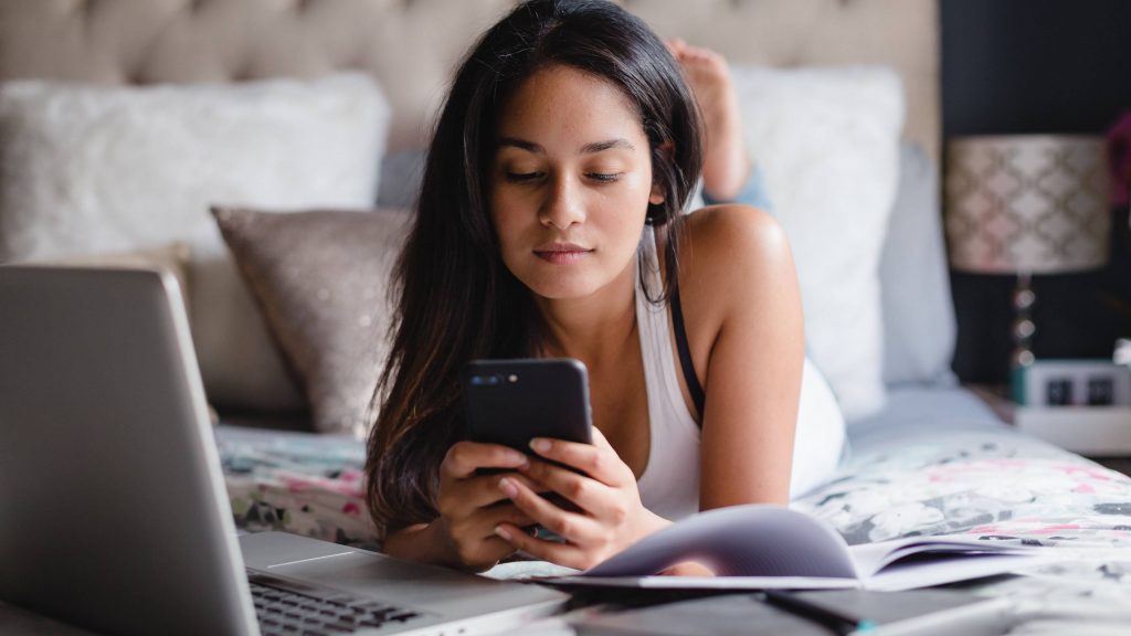 Una adolescente usa un teléfono inteligente y una computadora portátil en su habitación.