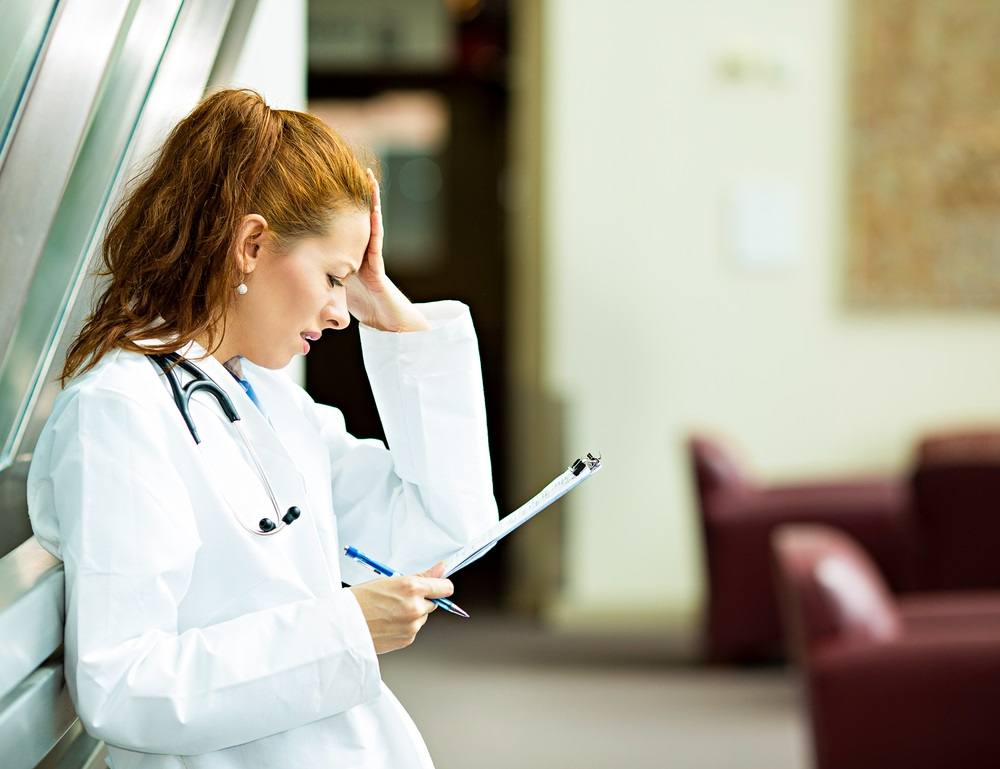 stressed female doctor with hand on head and holding clipboard