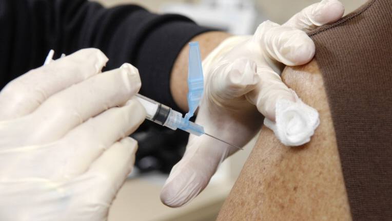 a Mayo Clinic medical staff person administering a flu shot in a Caucasian woman's sleeveless arm