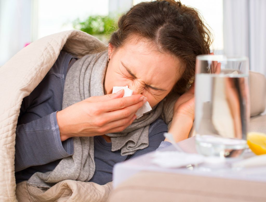 a middle aged woman sick in bed, sneezing into a tissue