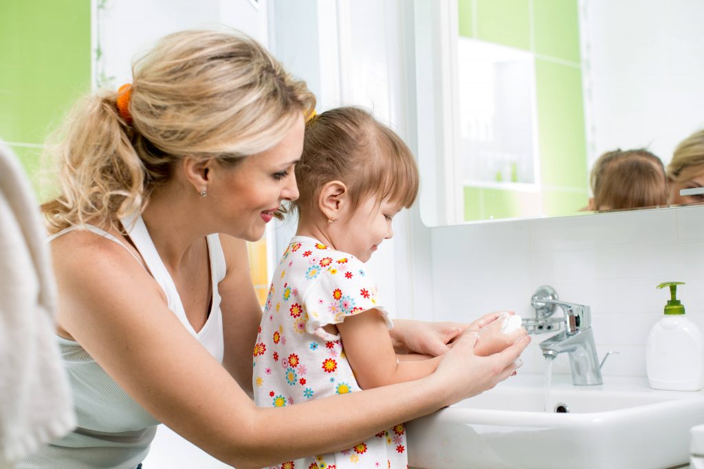 a young women with a child at a bathroom sink helping the little girl wash her hands