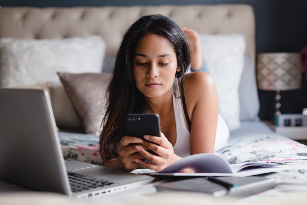 a teenage girl in her bedroom, using a smartphone and laptop