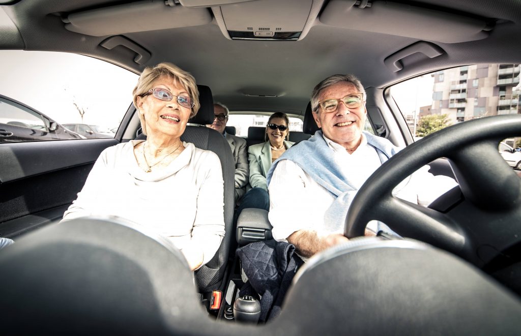 an elderly or senior man and woman driving in a car with a couple of friends in the back seat, laughing and smiling