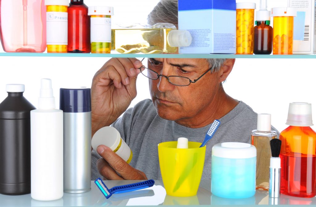 a middle-aged man reading a prescription bottle label in front of his open bathroom medicine cabinet