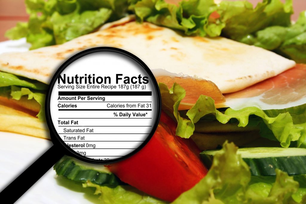 close up of a healthy vegetable sandwich with lettuce and tomato and a nutrition facts label under a microscope