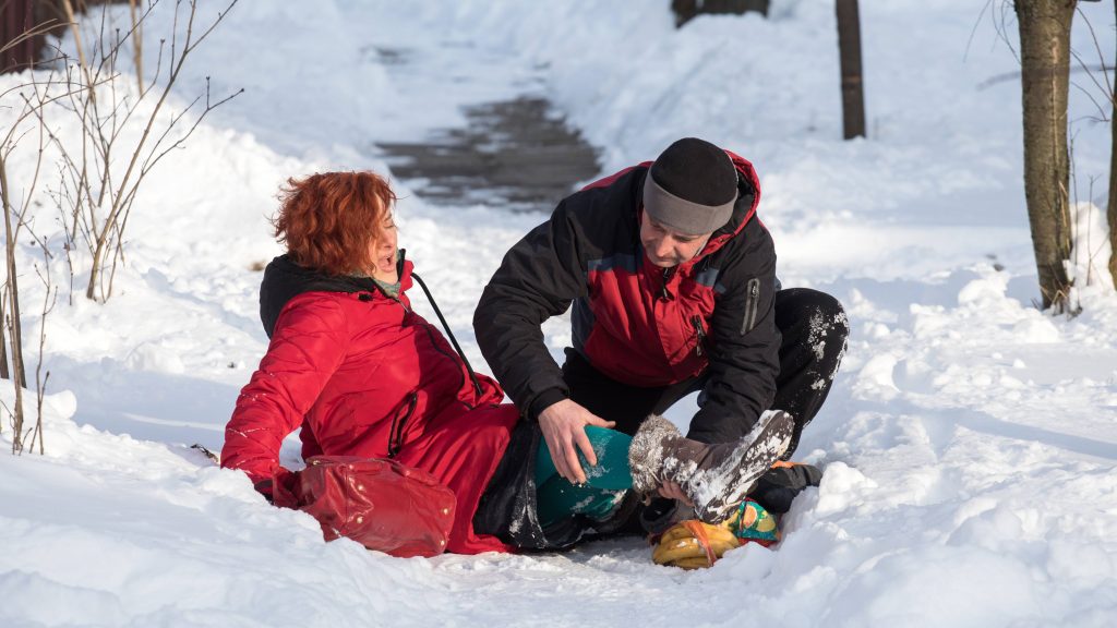 a woman who has fallen on a snowy, icy path in the winter woods and a male friend is helping her