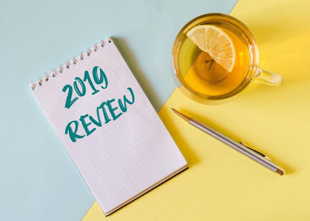a mug of tea with lemon, a pen, and a notebook with the words 2019 REVIEW