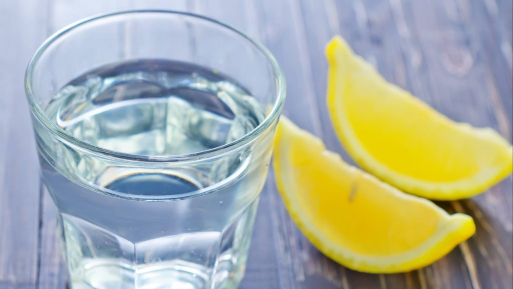 a glass of water sitting on a table with two slices of lemon nearby