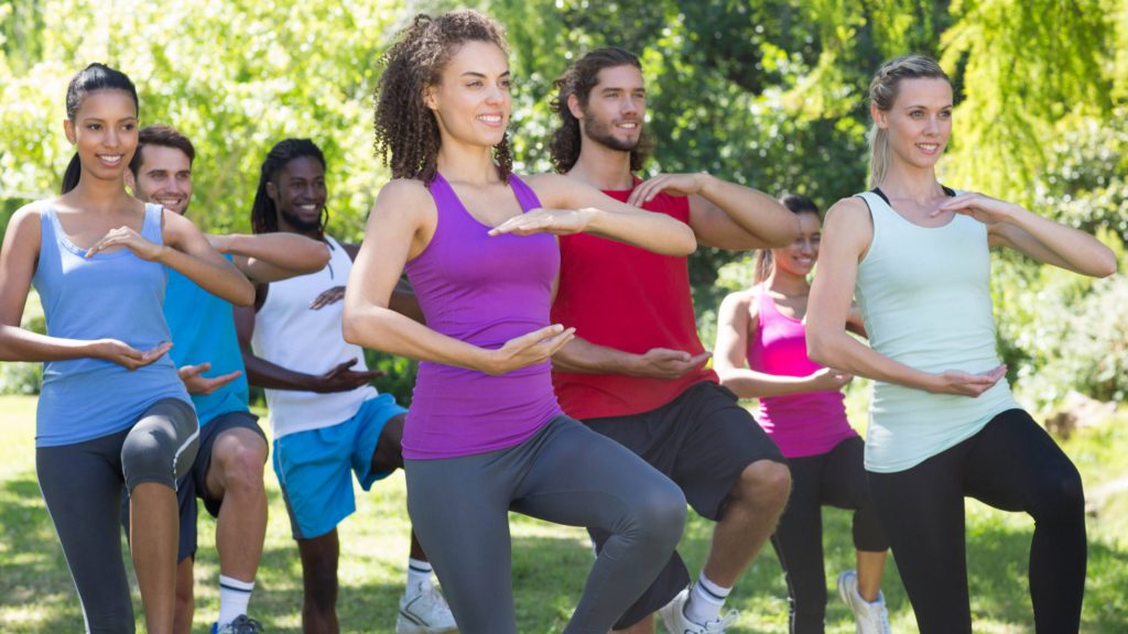 a group of people, athletes outside in a park stretching and exercising, perhaps doing yoga or Tai chi