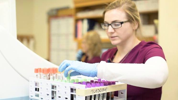a young white woman wearing glasses and medical gloves working in a research lab with blood samples