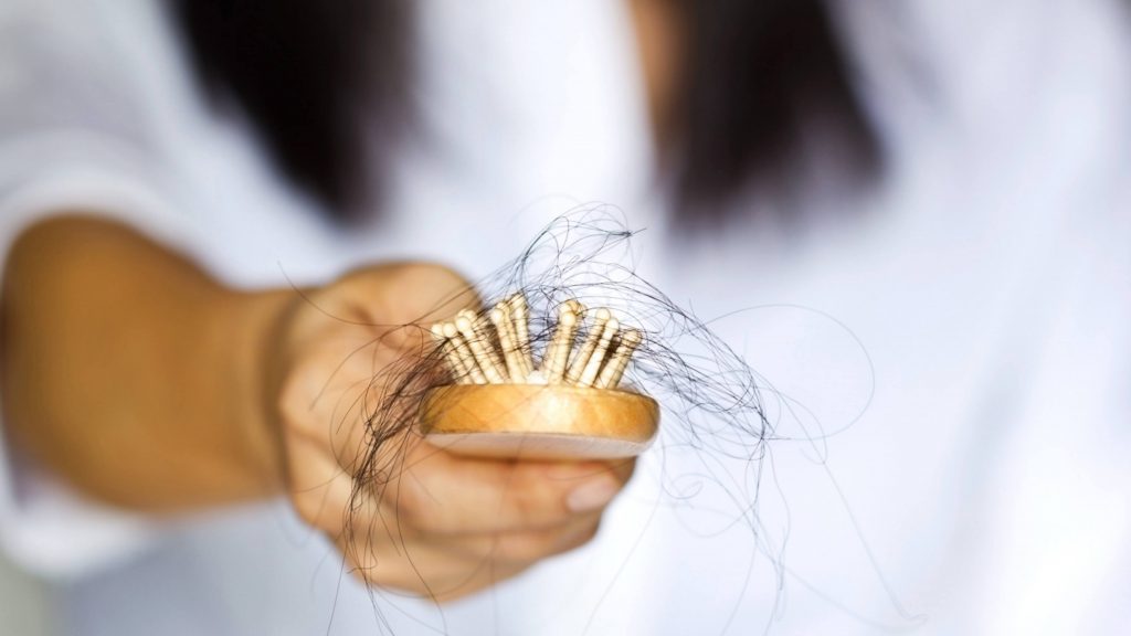 closeup of a woman's hand holding a hairbrush with clumps of hair representing hair loss