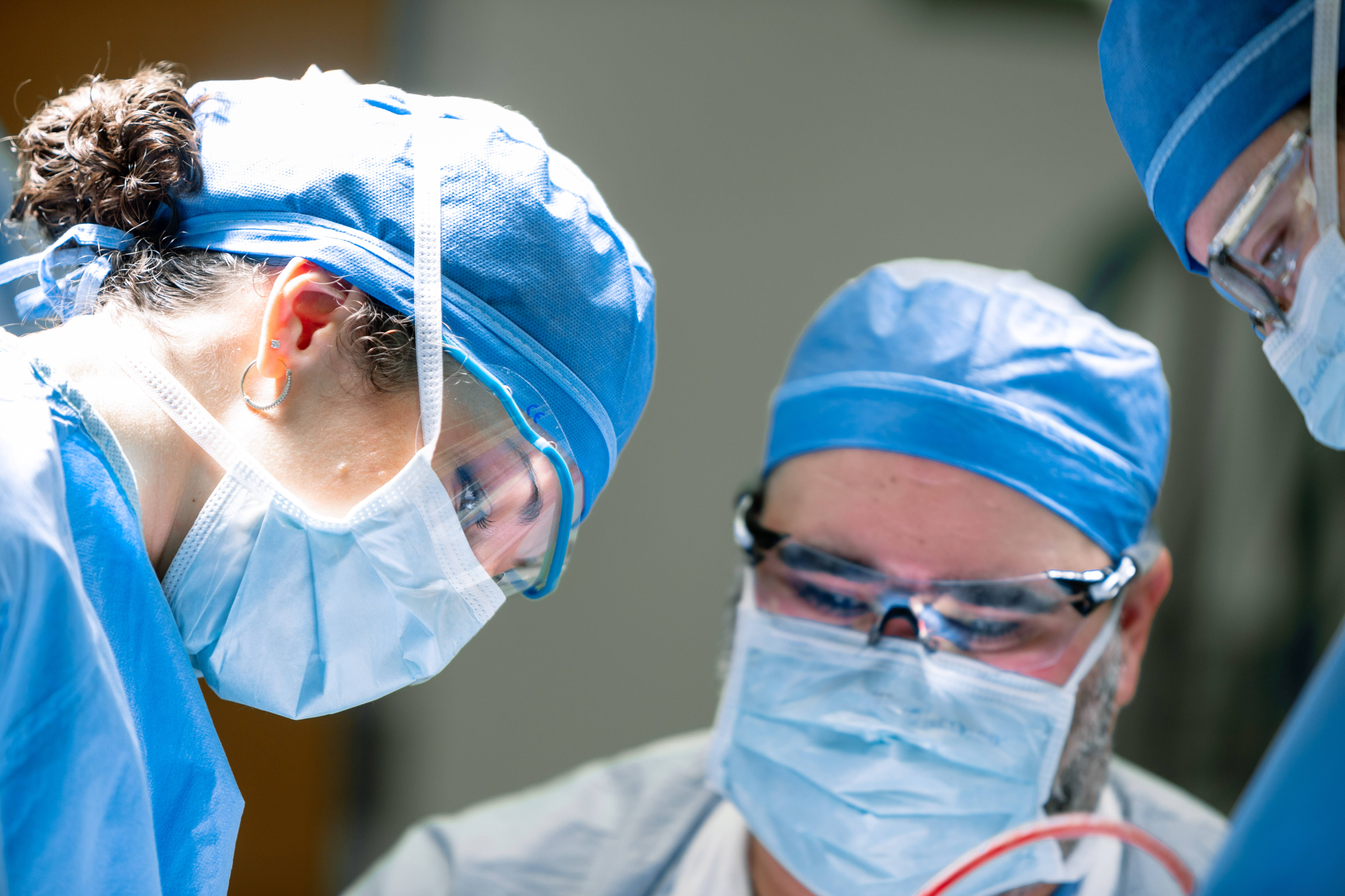 three surgeons operating on a patient while bending over