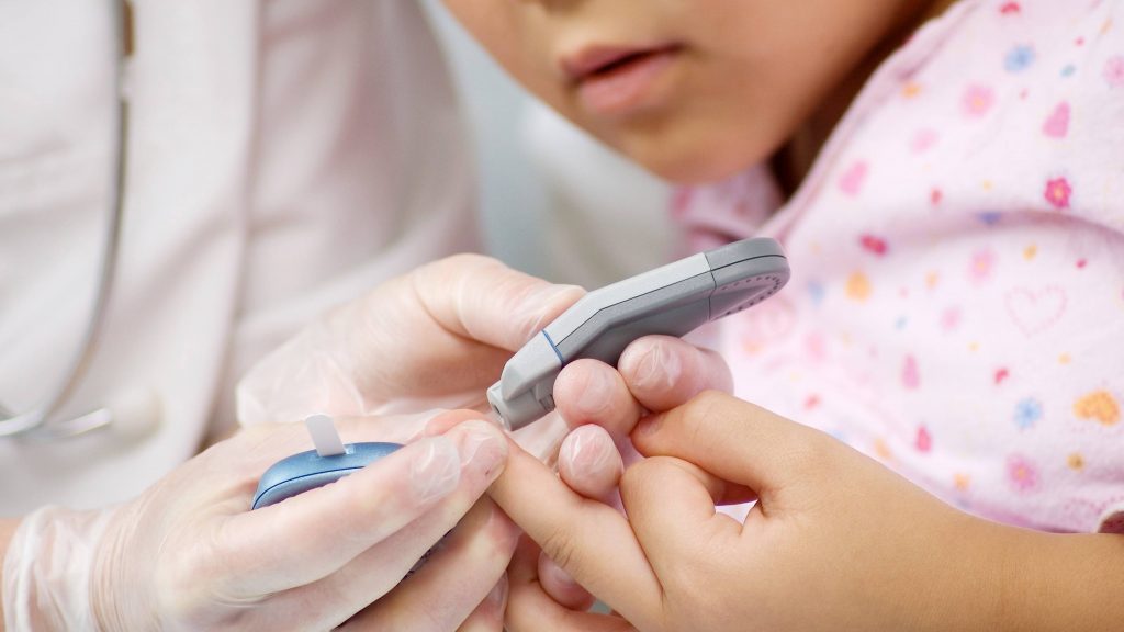 a young child, perhaps with diabetes, having a blood test administered by a medical staff person wearing gloves in a hospital or exam room