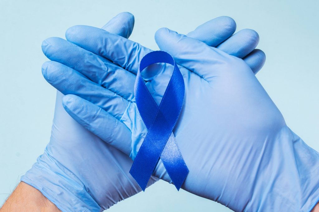 dos manos con guantes médicos azules sosteniendo una cinta azul para la concientización sobre el cáncer de colon