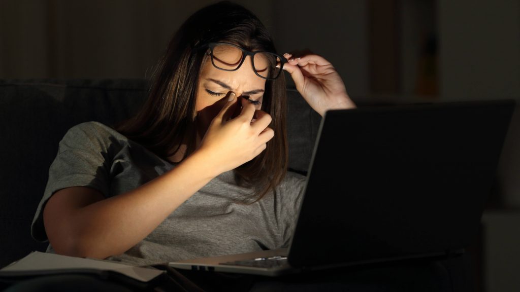 a young Caucasian woman up late at night, in the dark, wiping her eyes and on a computer looking tired, sleepy, sad, stressed, anxious