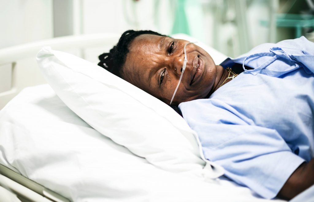 an African American woman slightly smiling in a hospital gown, resting on a pillow with oxygen tubes in her nose