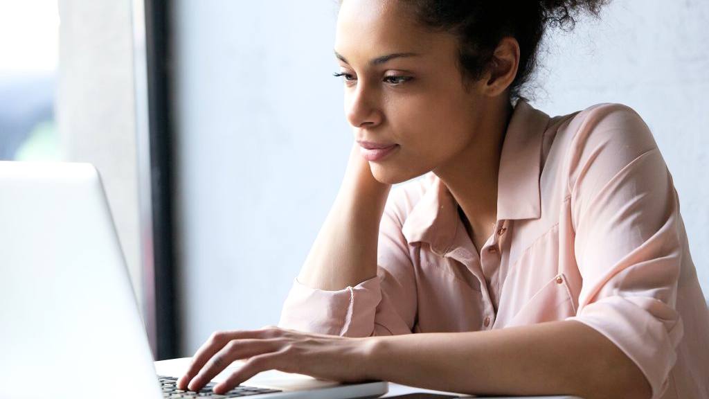 a young African American or Latina woman reading information on a laptop computer, looking thoughtful, serious