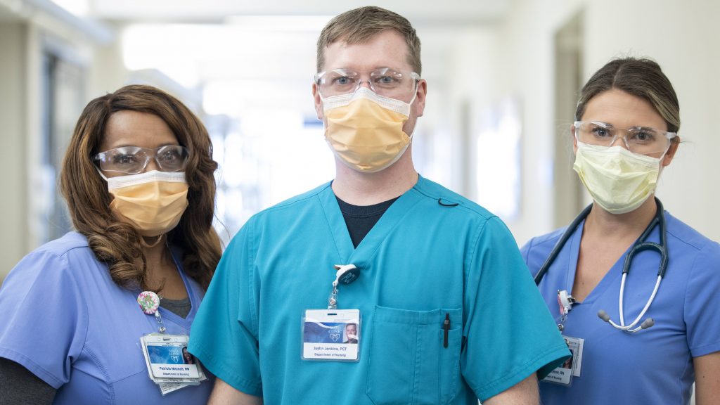three Mayo Clinic employees in medical scrubs wearing face masks and eye coverings