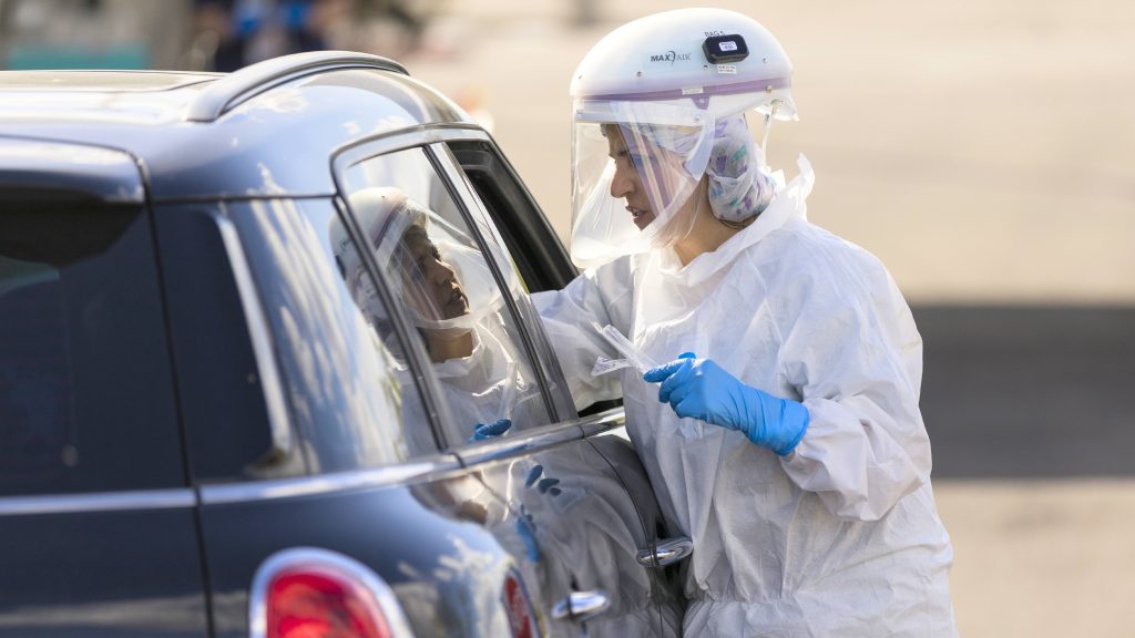 a Mayo Clinic medical staff person in Personal Protective Equipment, PPE, testing patients for COVID-19 who are in a car at a drive-up testing site