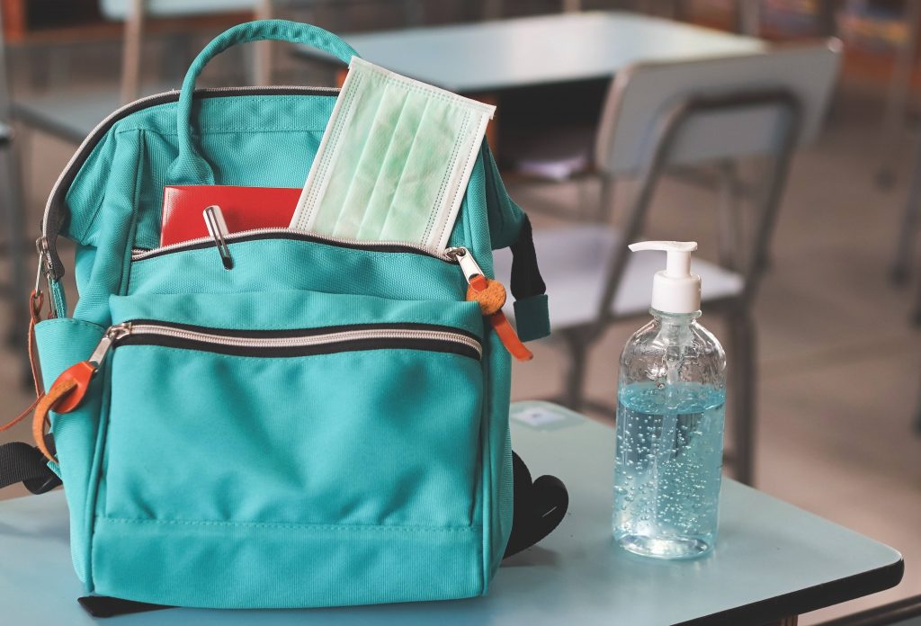 School backpack with mask tucked into pocket and hand sanitizer on desk