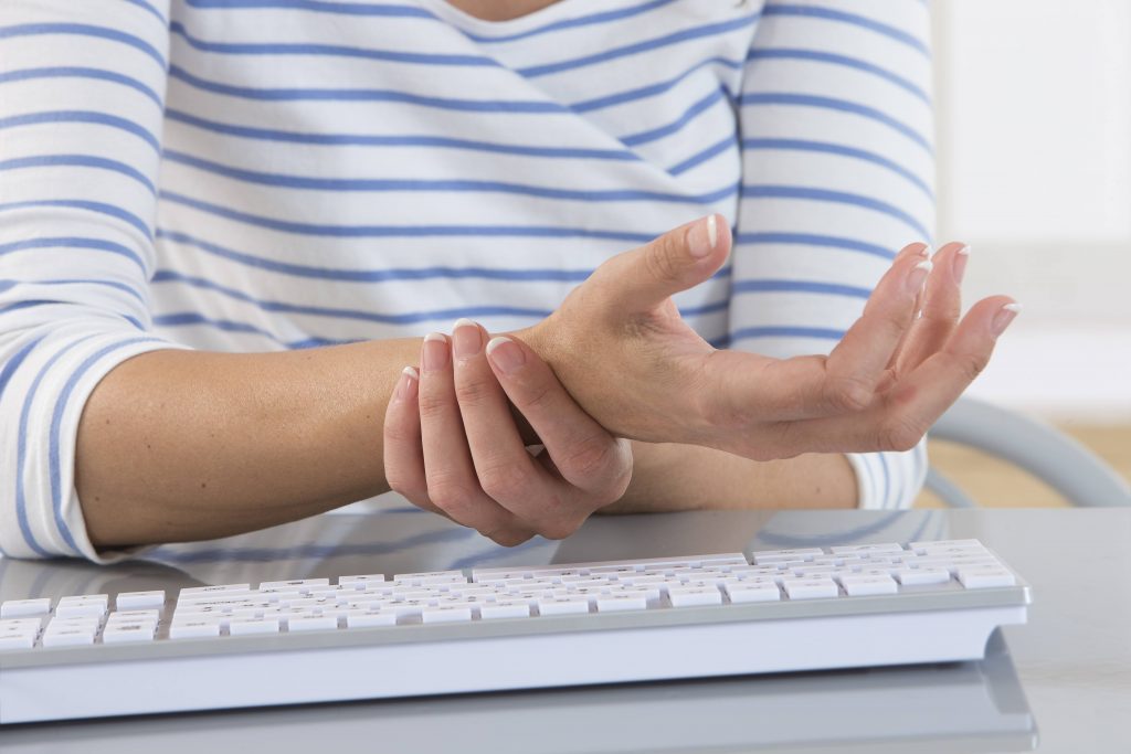 a white woman in a striped shirt near a computer keyboard holding her wrist because it's injured, sore, in pain