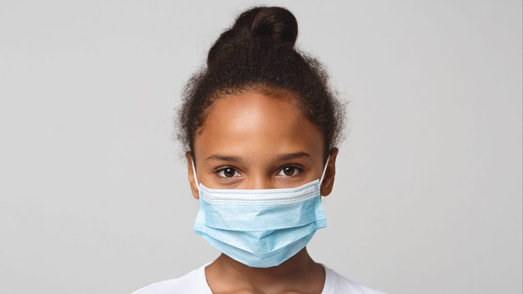a little Black school-aged girl with a plain white background and wearing a face mask