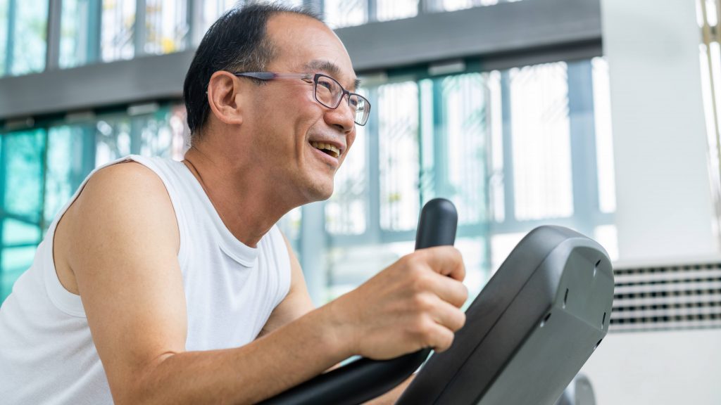 a middle aged Asian man wearing glasses and smiling while running and exercising on a treadmill