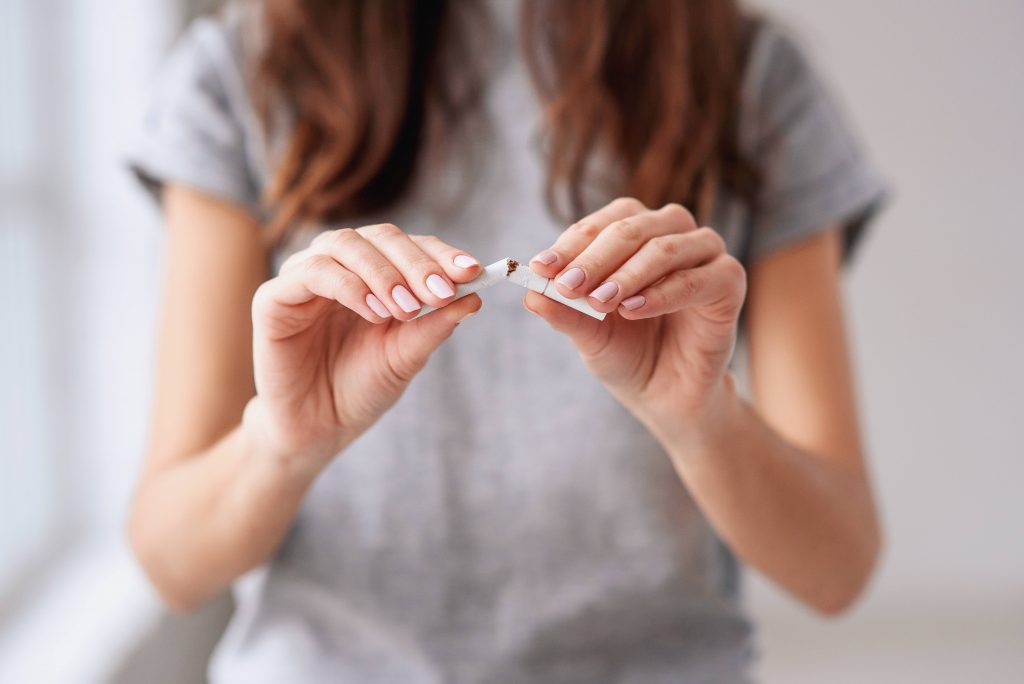 a young white woman in a t-shirt holding a cigarette and breaking it in half