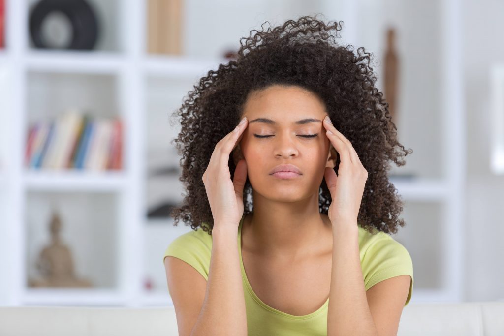 a young Black woman with her eyes closed and looking like she has a headache, or is medicating, rubbing her forehead, headaches.